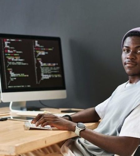 Young black man in casualwear keeping hands on computer keyboard while sitting in front of monitors _ Premium Photo