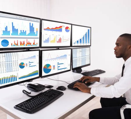 young businessman analyzing financial chart on multiple computers in office
