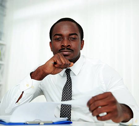 pensive african man sitting at the table and signing document in office