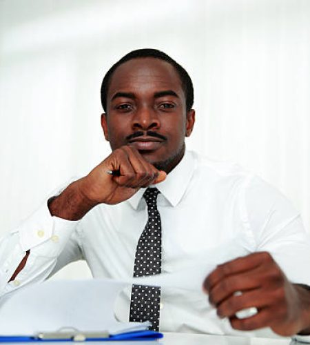 pensive african man sitting at the table and signing document in office